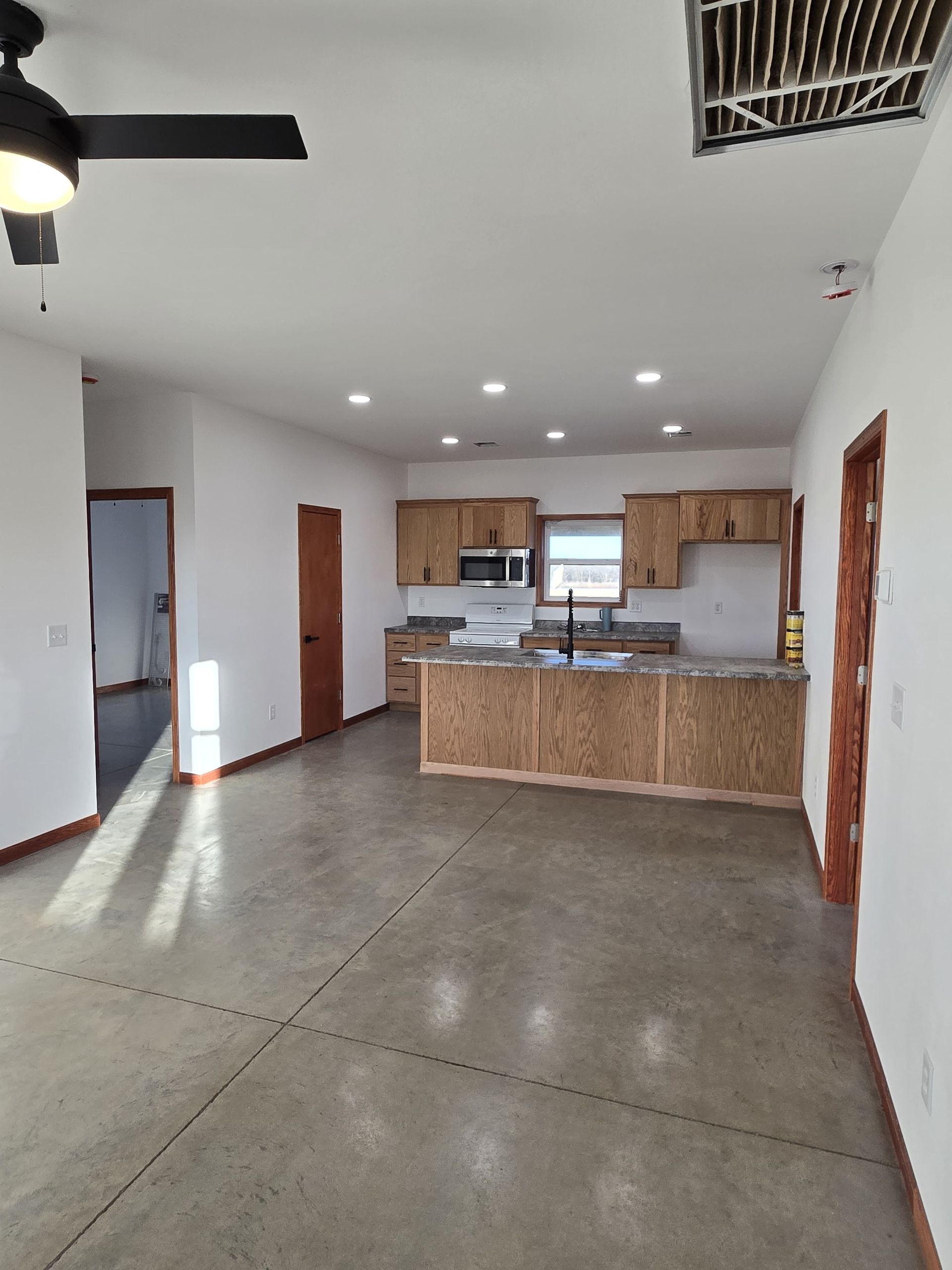 An open-concept room with a kitchen featuring light wood cabinets and a counter, and gray concrete flooring.
