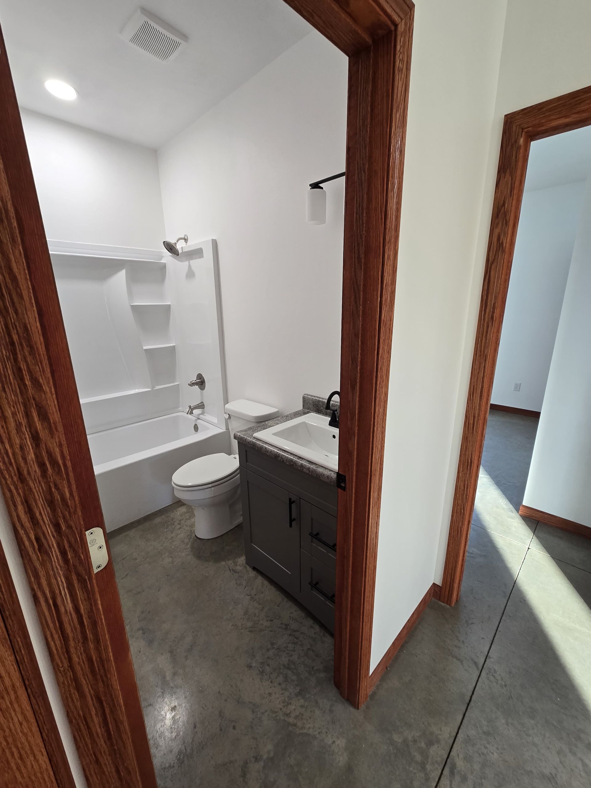 A small bathroom with a gray vanity, white toilet, and tub-shower combo, viewed through a wooden door frame.