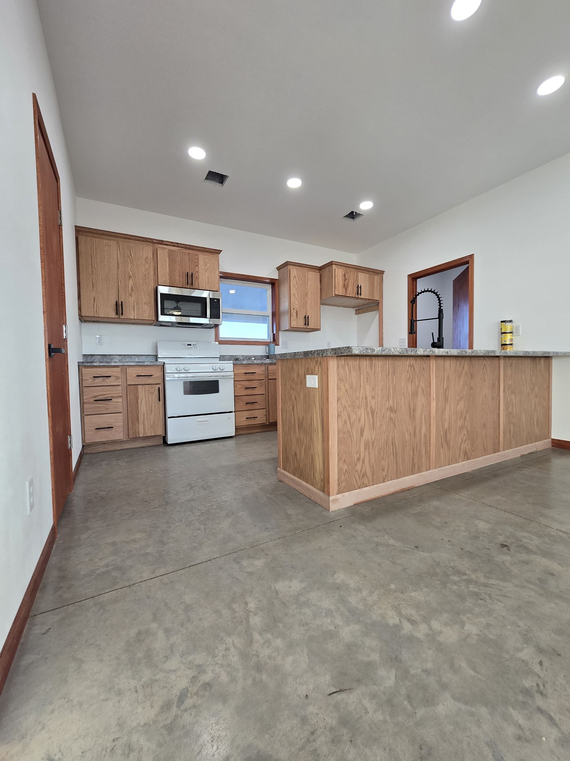 A modern kitchen with oak cabinets, a white stove, a large center island, and polished concrete floors.