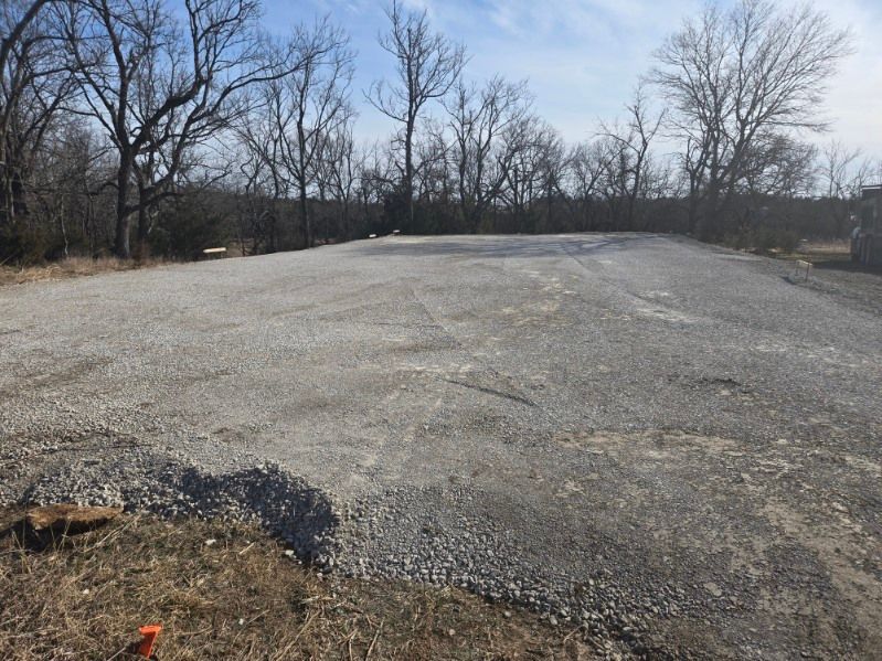 A wide, level gravel pad or parking area bordered by trees under a clear blue sky.