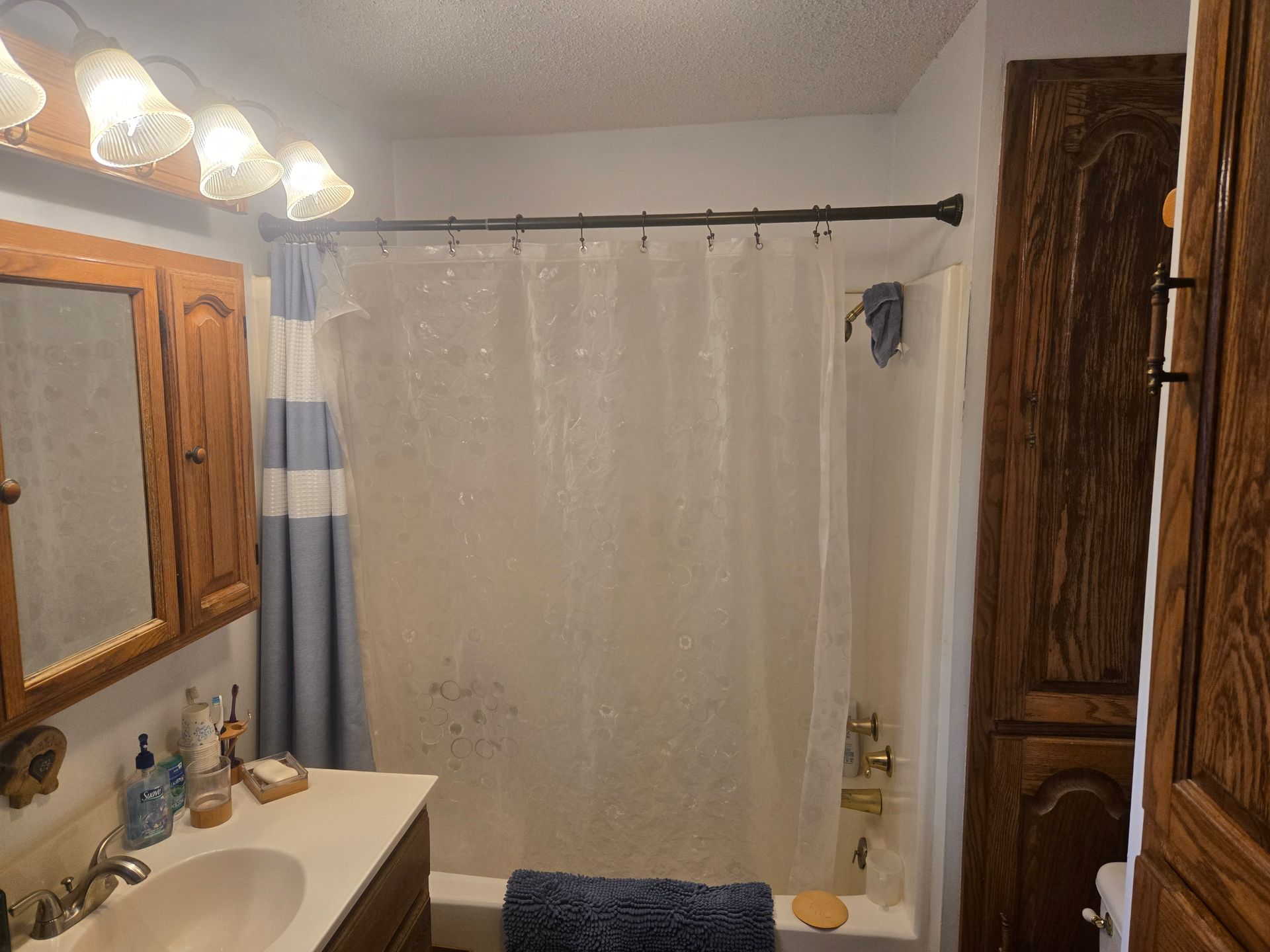 A bathroom featuring a wooden vanity, a sink, a medicine cabinet, a bathtub with a white shower curtain, and wood cabinets.