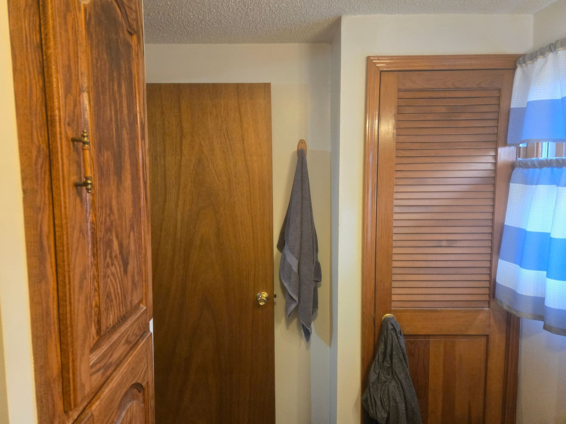 A hallway featuring wooden cabinets and doors, with two gray towels hanging from hooks against light-colored walls.