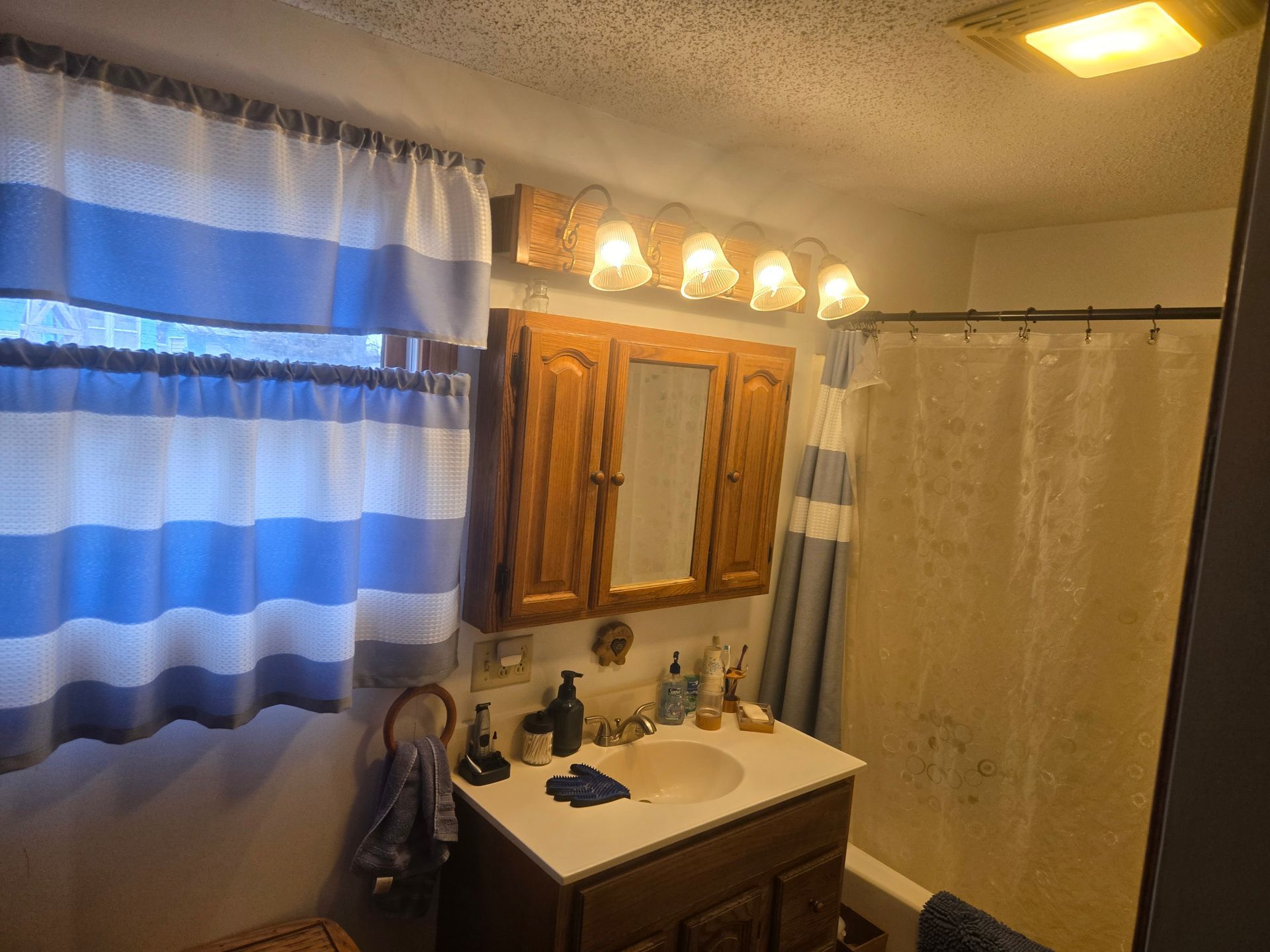A bathroom with blue-and-white striped curtains, a wooden cabinet, vanity sink, and a shower curtain.