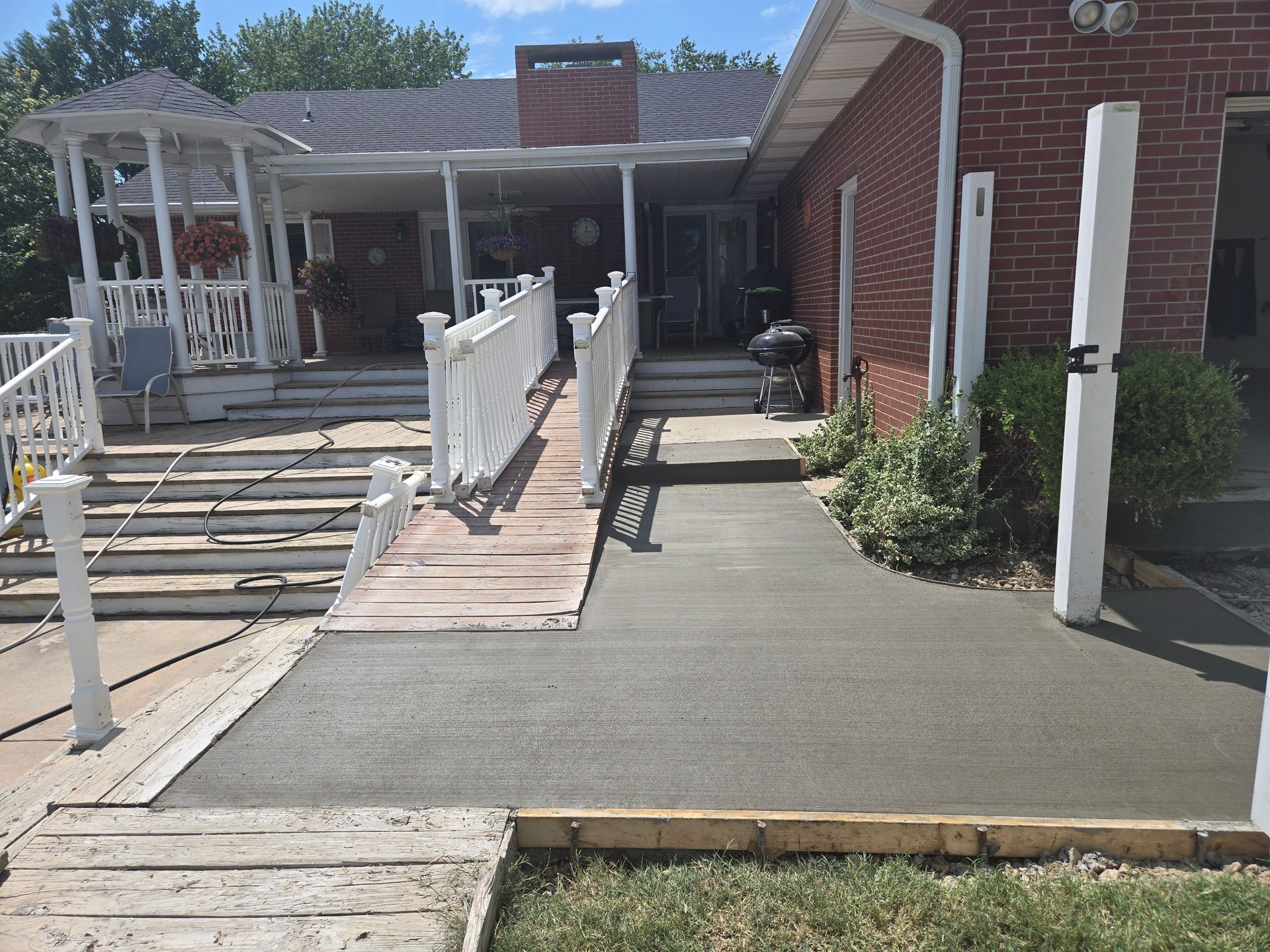 People smoothing wet concrete with trowels to create a sidewalk. They're working in a dirt area with wooden forms.