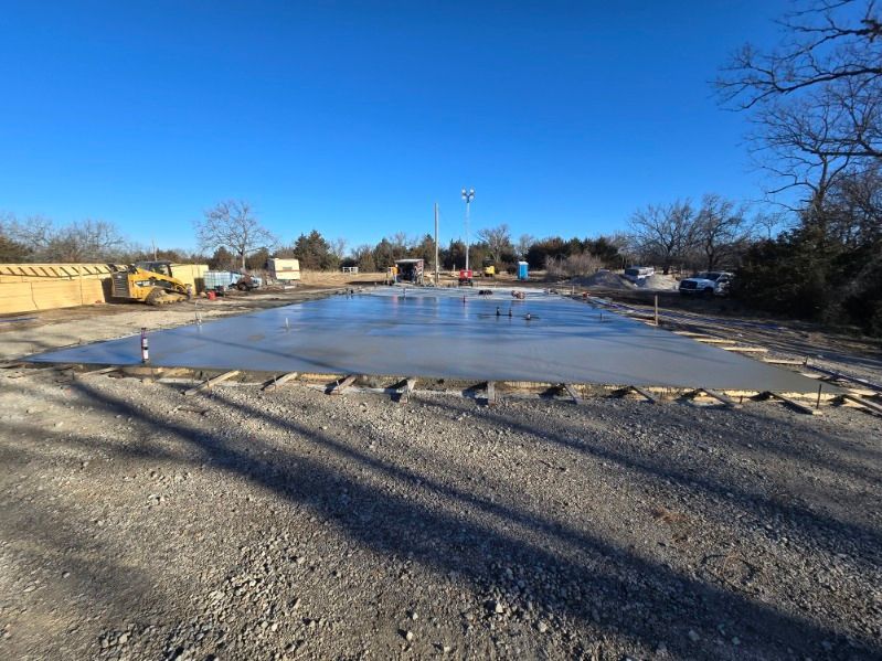 Freshly poured concrete slab for a new building construction site under a clear blue sky.