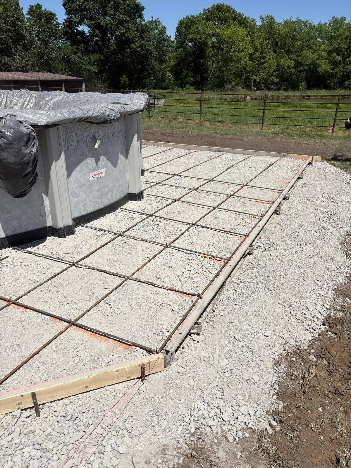 Concrete patio foundation with rebar grid and gravel border beside a stone structure outdoors