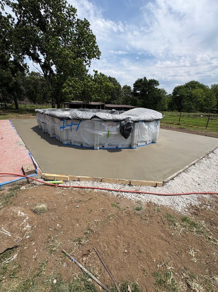 Circular concrete structure in a rural field, with tarps draped over the top and trees in the background