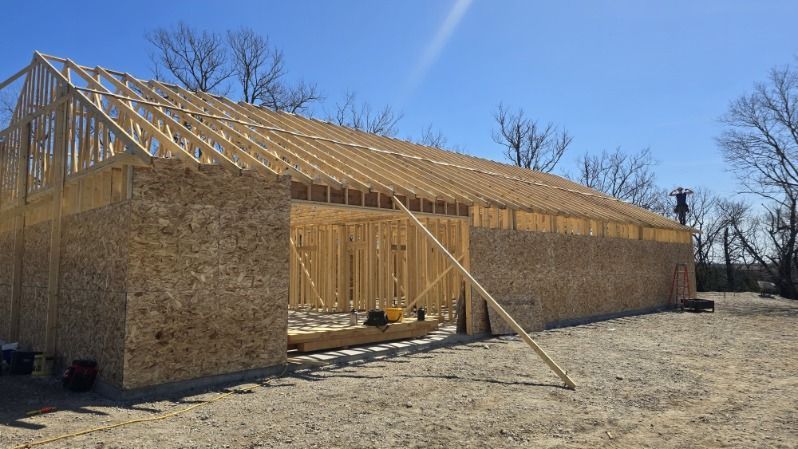 Wood-framed house under construction with plywood walls and roof trusses in a dry, open lot