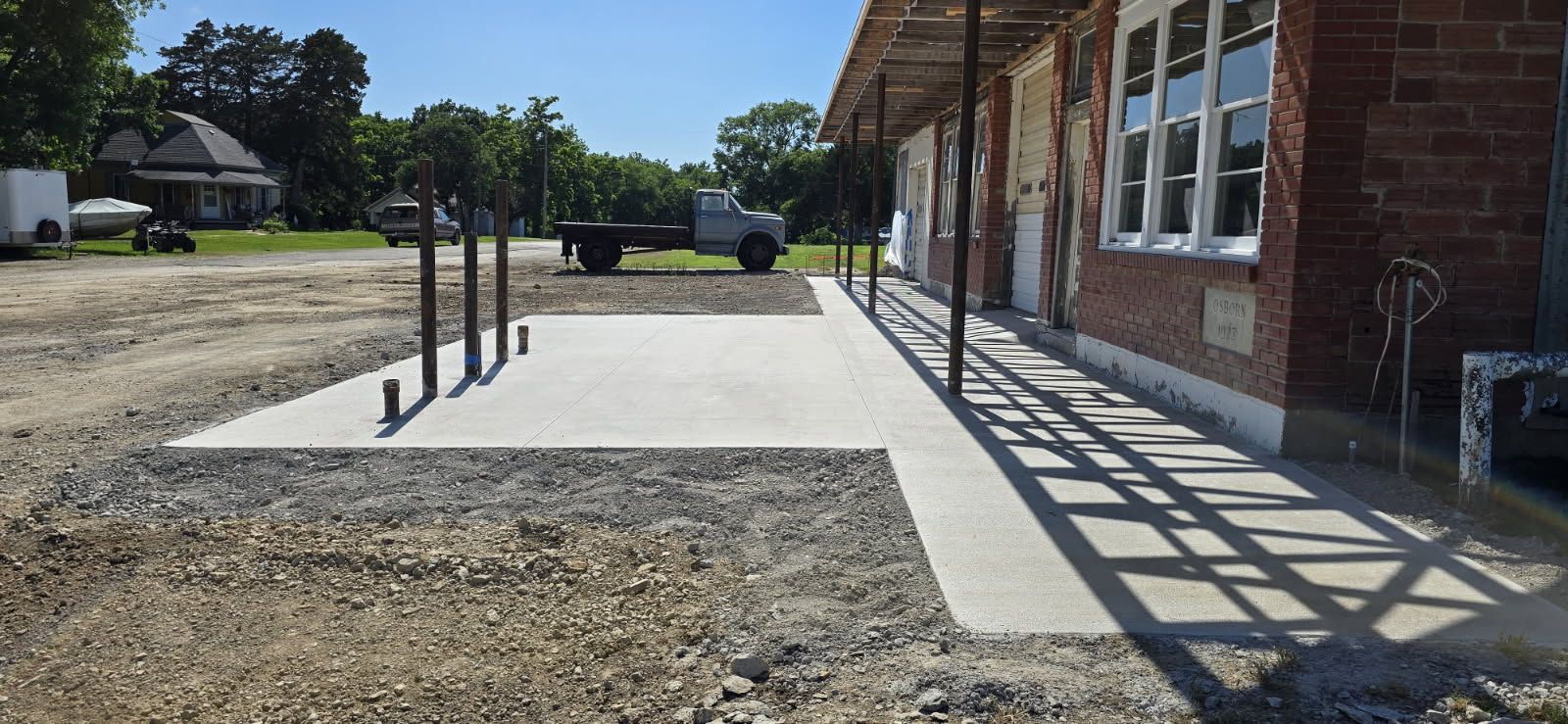 Concrete sidewalk beside a brick building, with metal handrails and a shaded walkway in front.