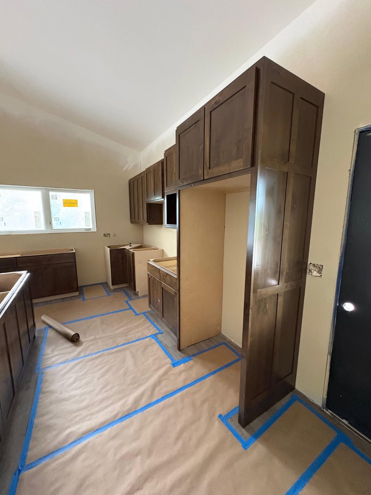 Renovated room with brown cabinets, blue floor tape, and a window on the left