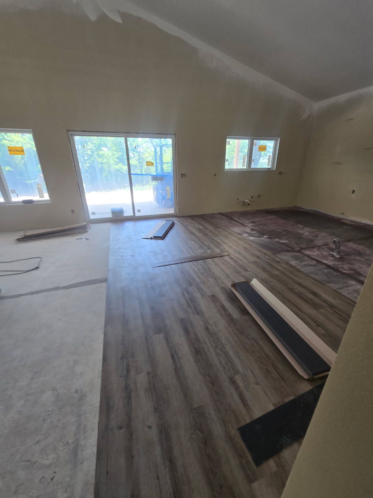 Empty room with wood flooring being installed and sliding glass doors at the back.