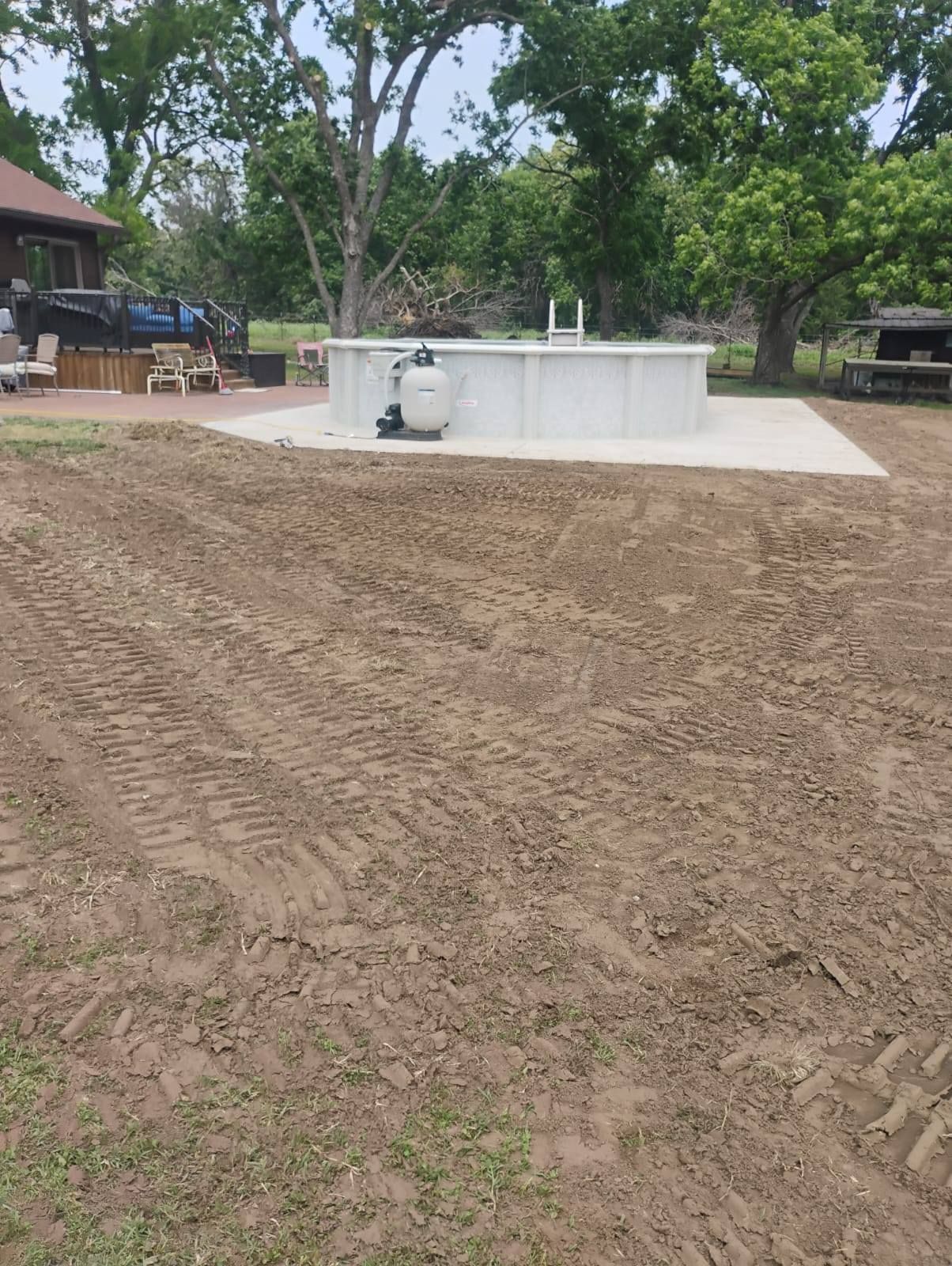 Backyard with a concrete pool or patio under construction, surrounded by dirt and trees