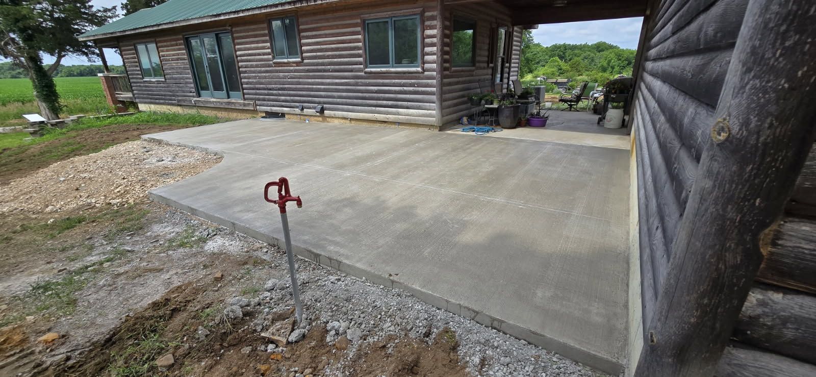 Concrete patio beside a log cabin, with a red-handled valve in the foreground and yard in the background