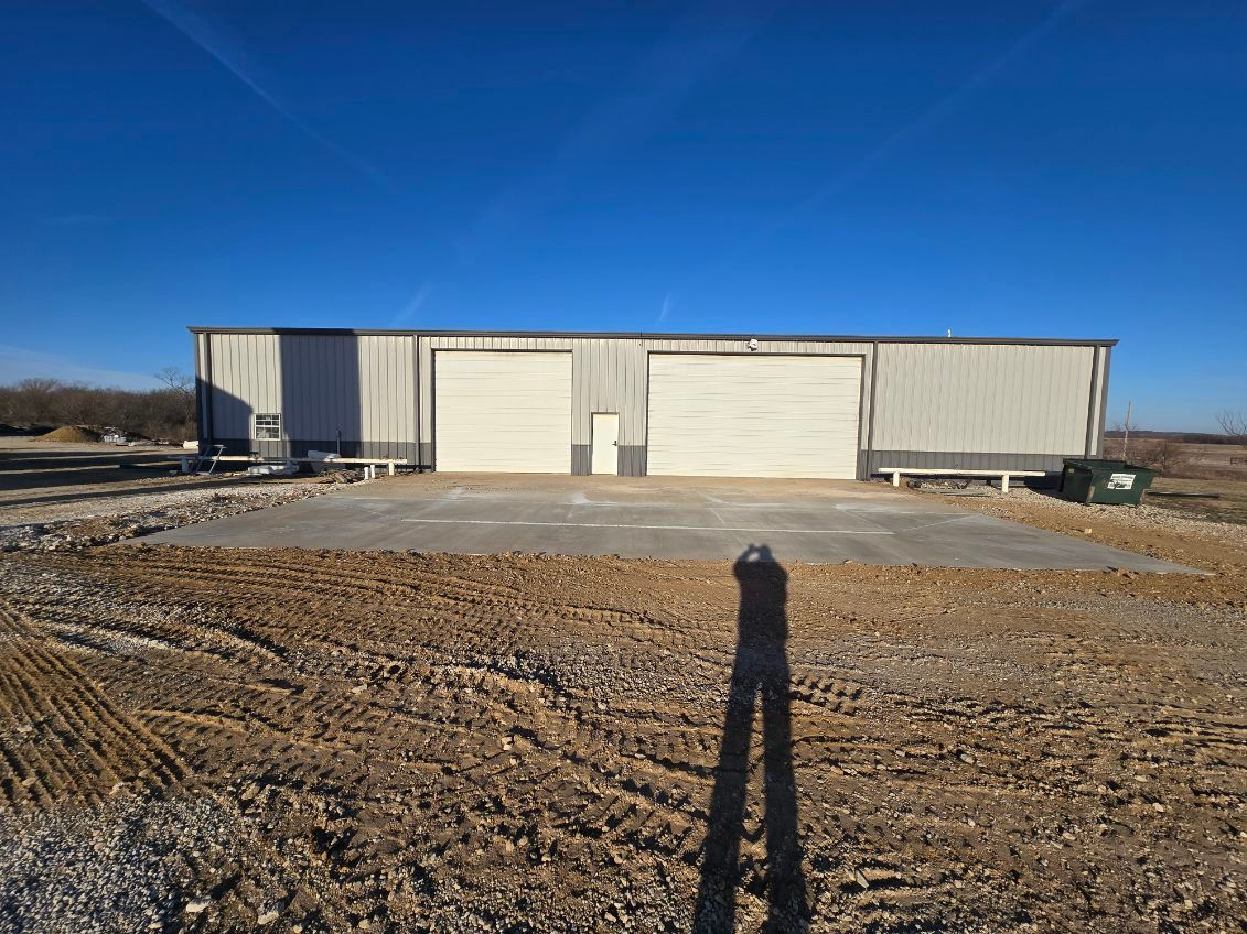 A metal warehouse building with two large roll-up doors and a center entrance, fronted by a new concrete pad.