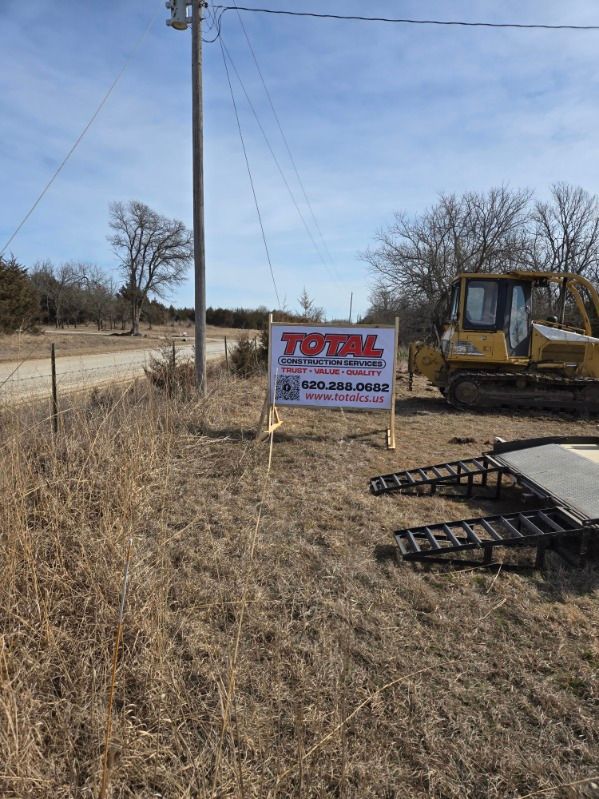 A Total Land Management sign stands in a field next to a yellow bulldozer and trailer on a sunny day.