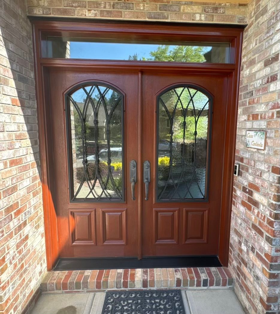 The front door of a brick house with a wooden door and glass windows.