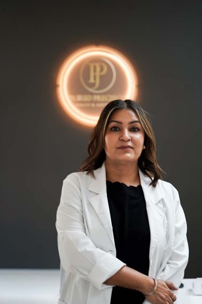Woman in white coat stands in front of a logo with a golden halo.