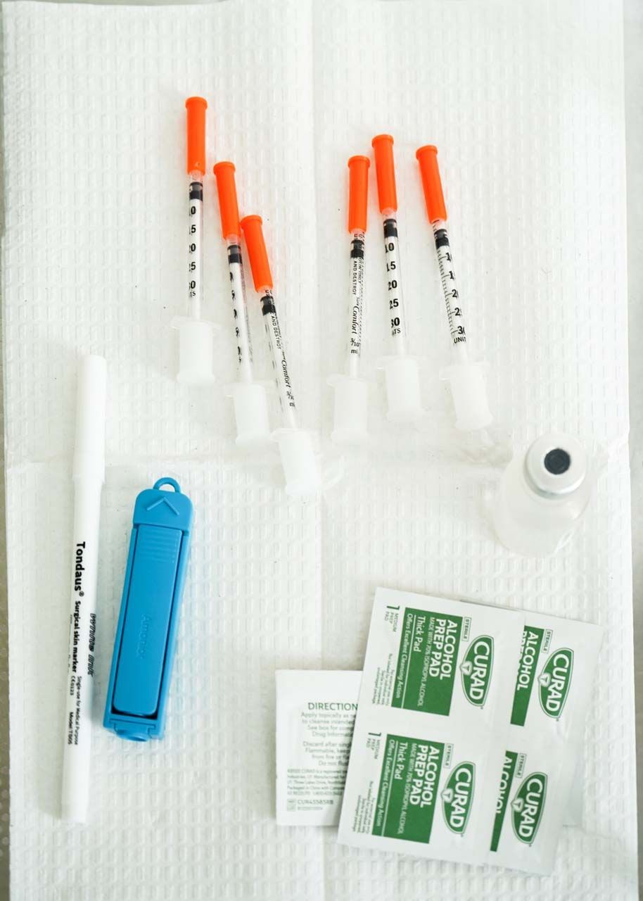 Medical supplies laid out on a white surface, including syringes, alcohol pads, and insulin pen.