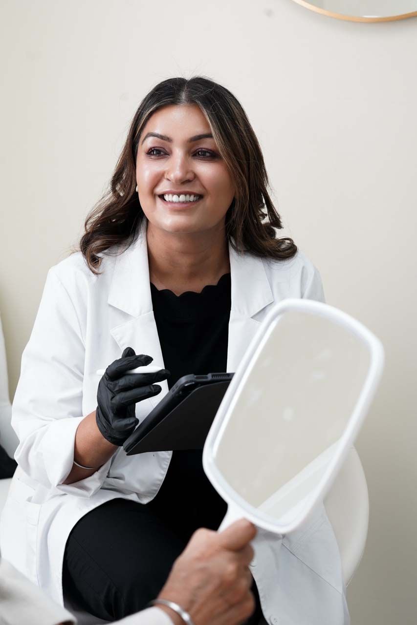 A person in a white lab coat with black gloves looking at a mirror, smiling.