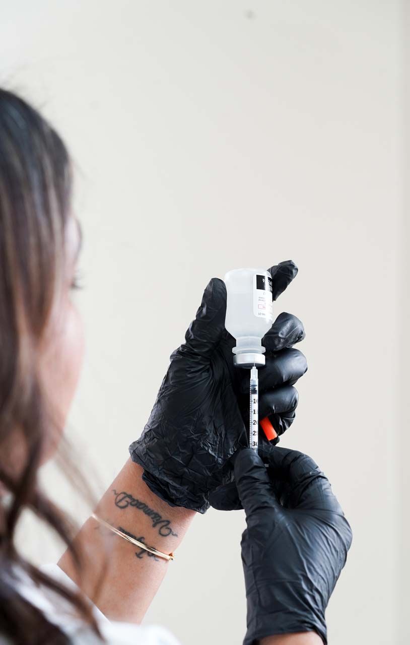 Person wearing black gloves drawing medicine into a syringe from a vial.