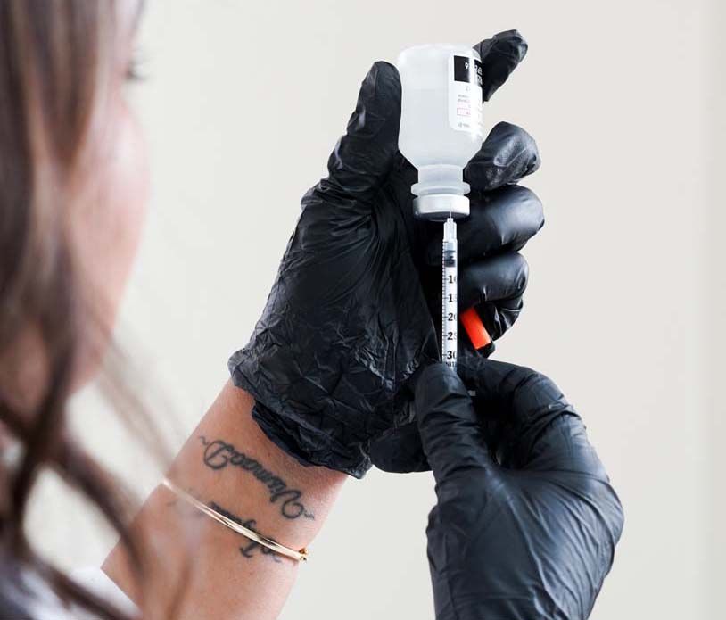 Person wearing black gloves drawing liquid from a vial into a syringe.