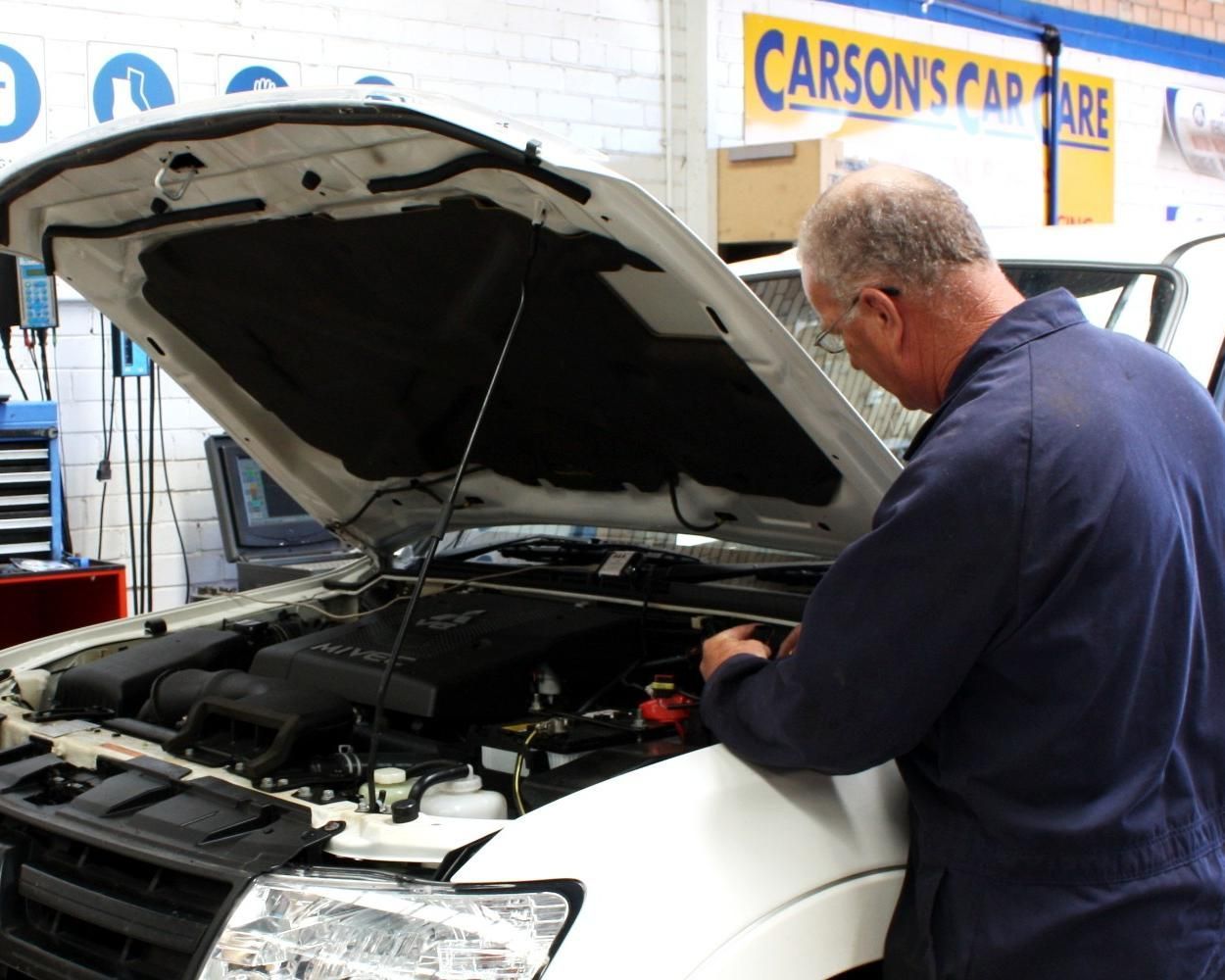 A Man Is Working On A Car With The Hood Open In Front Of A Carson 's Car Care Sign — Carson's Car Care In Armidale, NSW