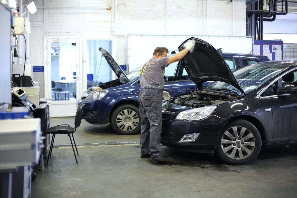 A Man Is Working On A Car In A Garage With The Hood Open — Carson's Car Care In Armidale, NSW