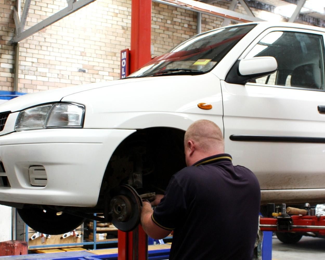 A Man Is Working On A White Car In A Garage — Carson's Car Care In Armidale, NSW