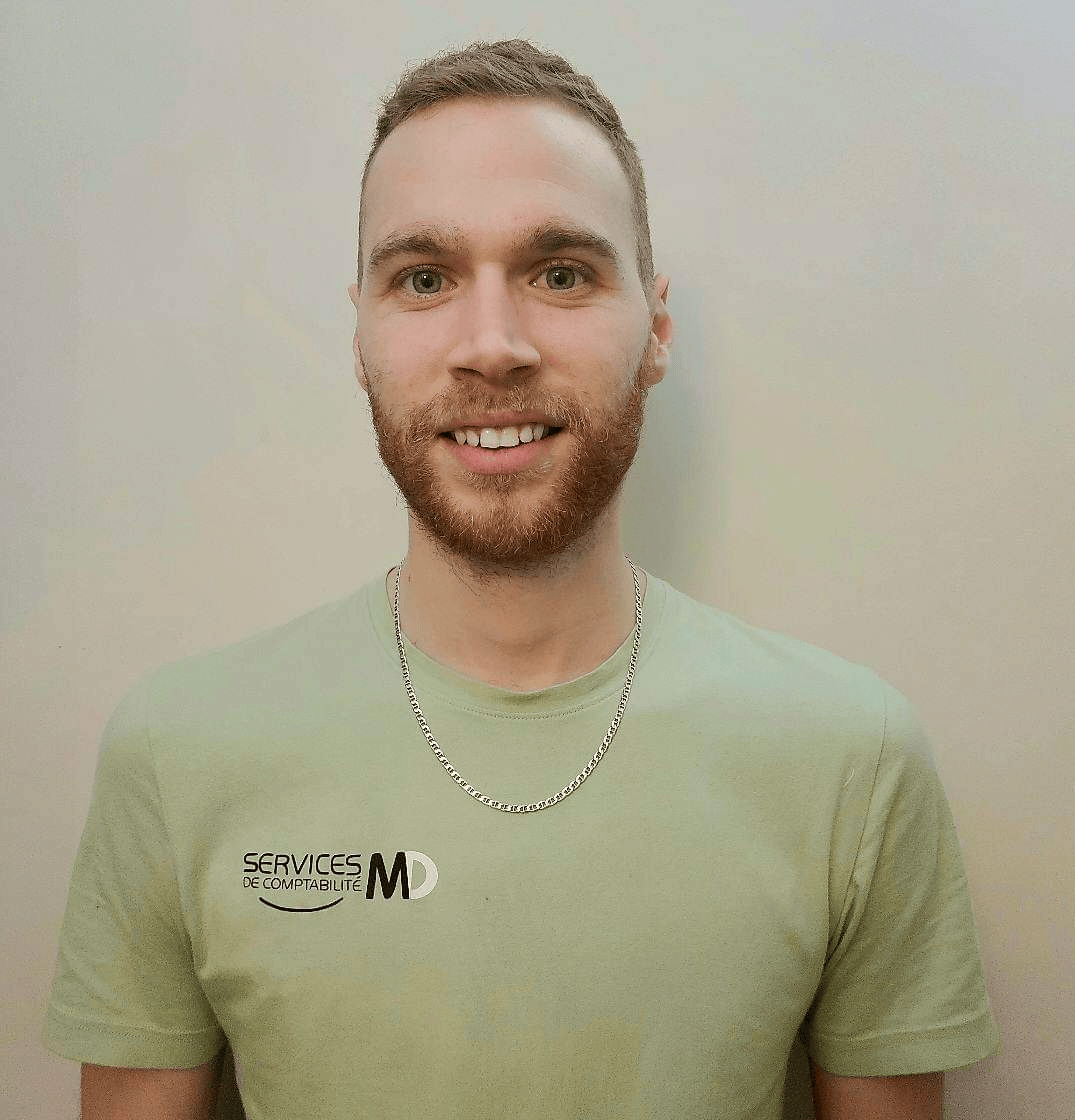 Man with a red beard smiling, wearing a light green shirt and a necklace. Neutral background.