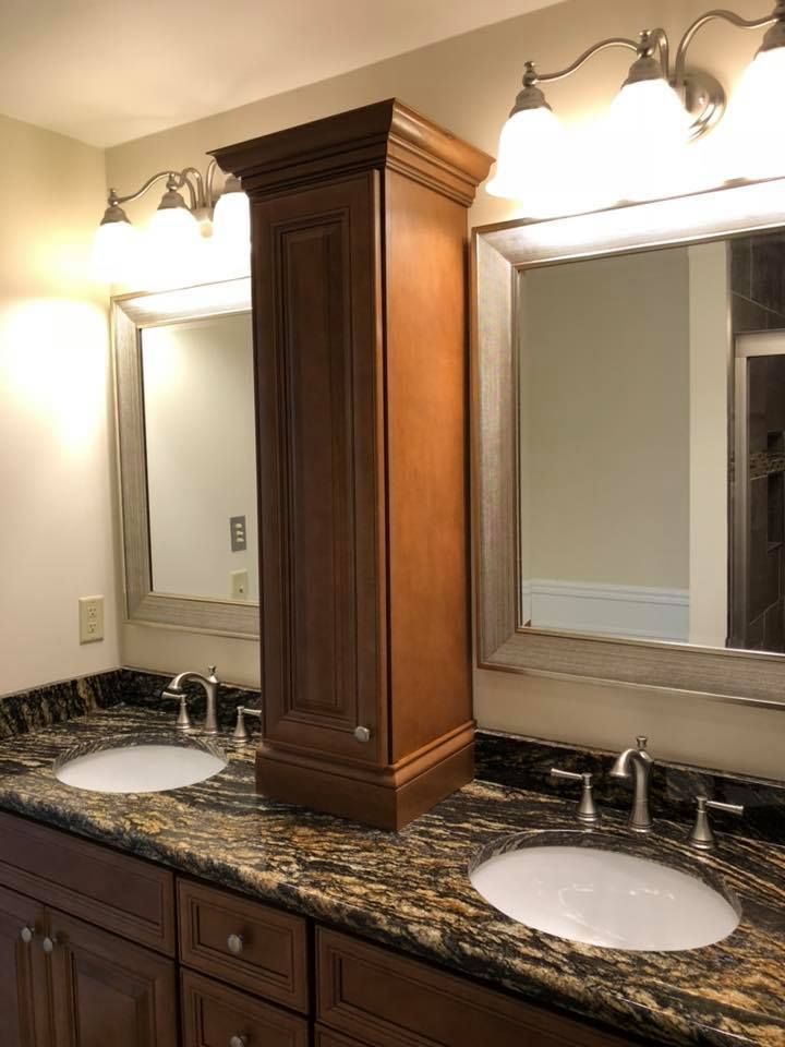 Bathroom with two sinks, mirrors, and a tall cabinet; brown and gold granite countertop.