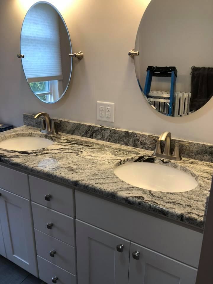 Double vanity with white cabinets, gray granite countertop, oval mirrors, and brushed nickel faucets.