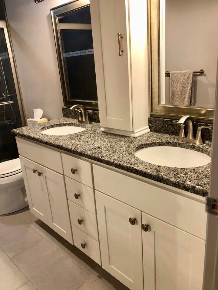 White bathroom vanity with two sinks, granite countertop, and cabinet.