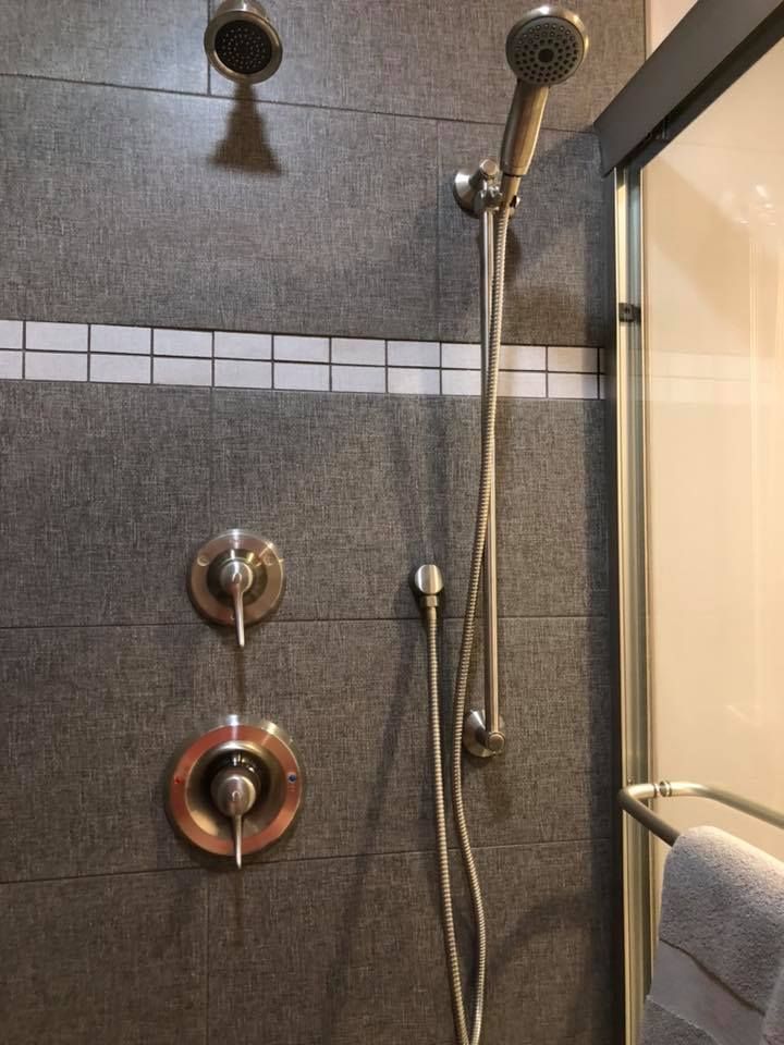 Shower with gray tile, two showerheads, and silver faucet controls. A towel hangs nearby.