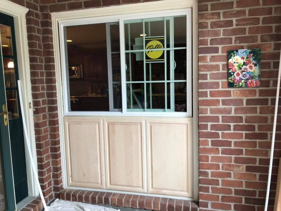 Window with security bars and wooden paneling on a red brick wall. A floral plaque hangs to the right.
