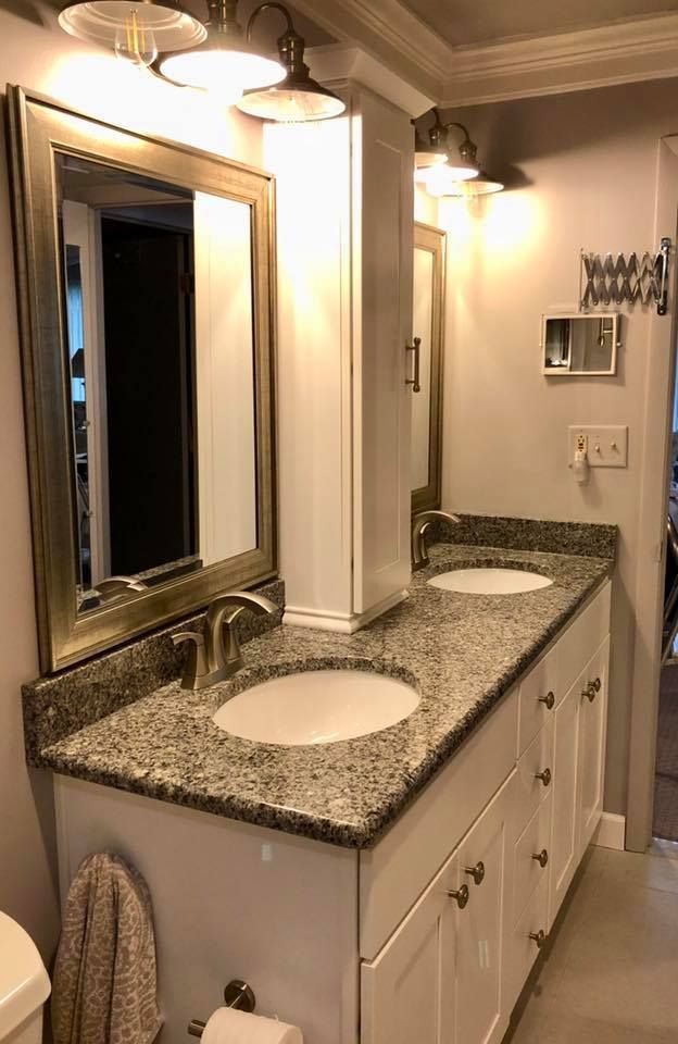 Bathroom with a white vanity, granite countertop, two sinks, mirror, and cabinet.