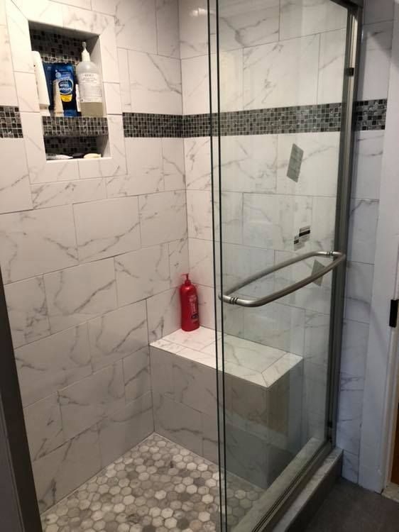 A tiled shower with a glass door, built-in seat, and a shelf for toiletries.