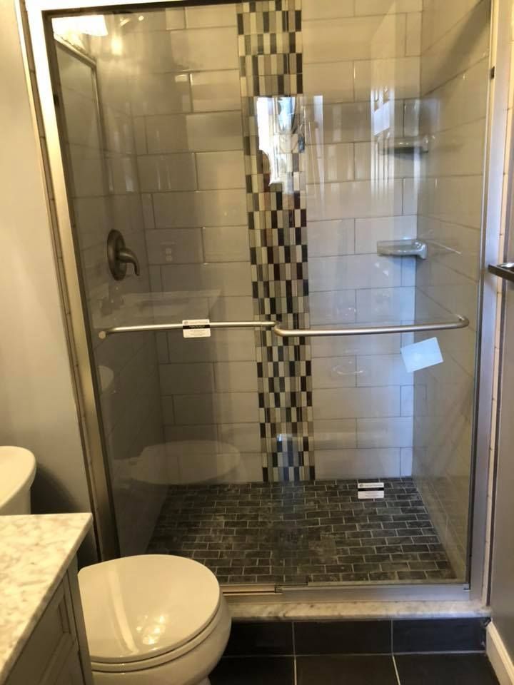 Shower stall with glass doors, gray and black tile, chrome fixtures.