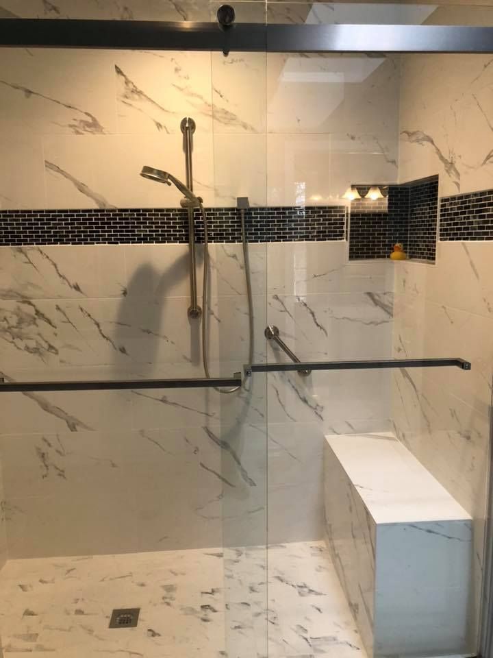 Shower with marble tile walls, sliding glass door, bench, and black accents.