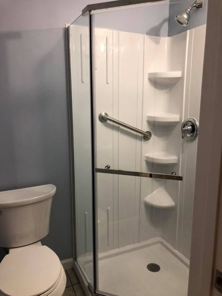 Bathroom with a white corner shower, toilet, and light blue wall. A grab bar is mounted inside the shower.