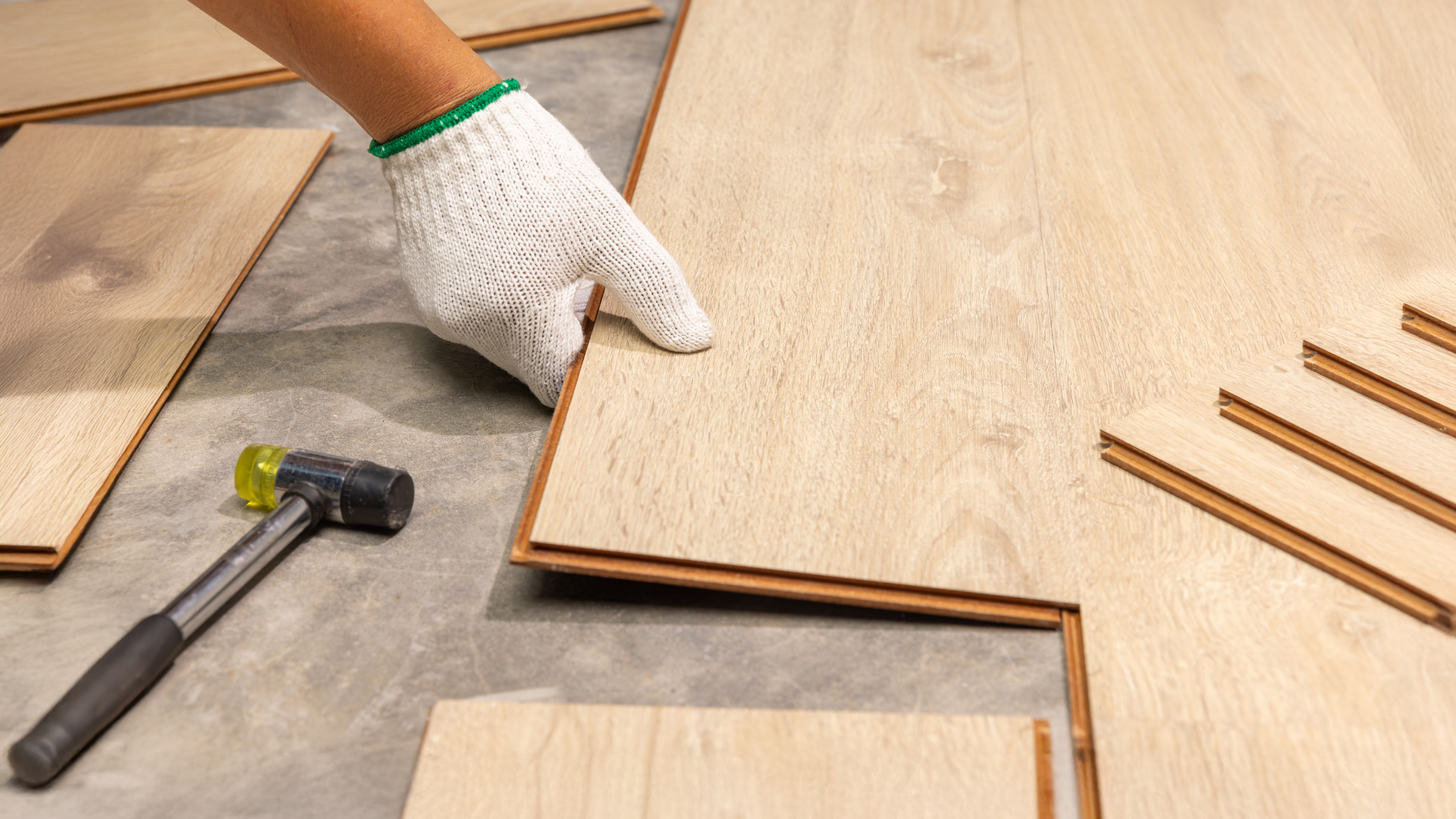 Person in white glove fitting wood floor planks. Hammer nearby.