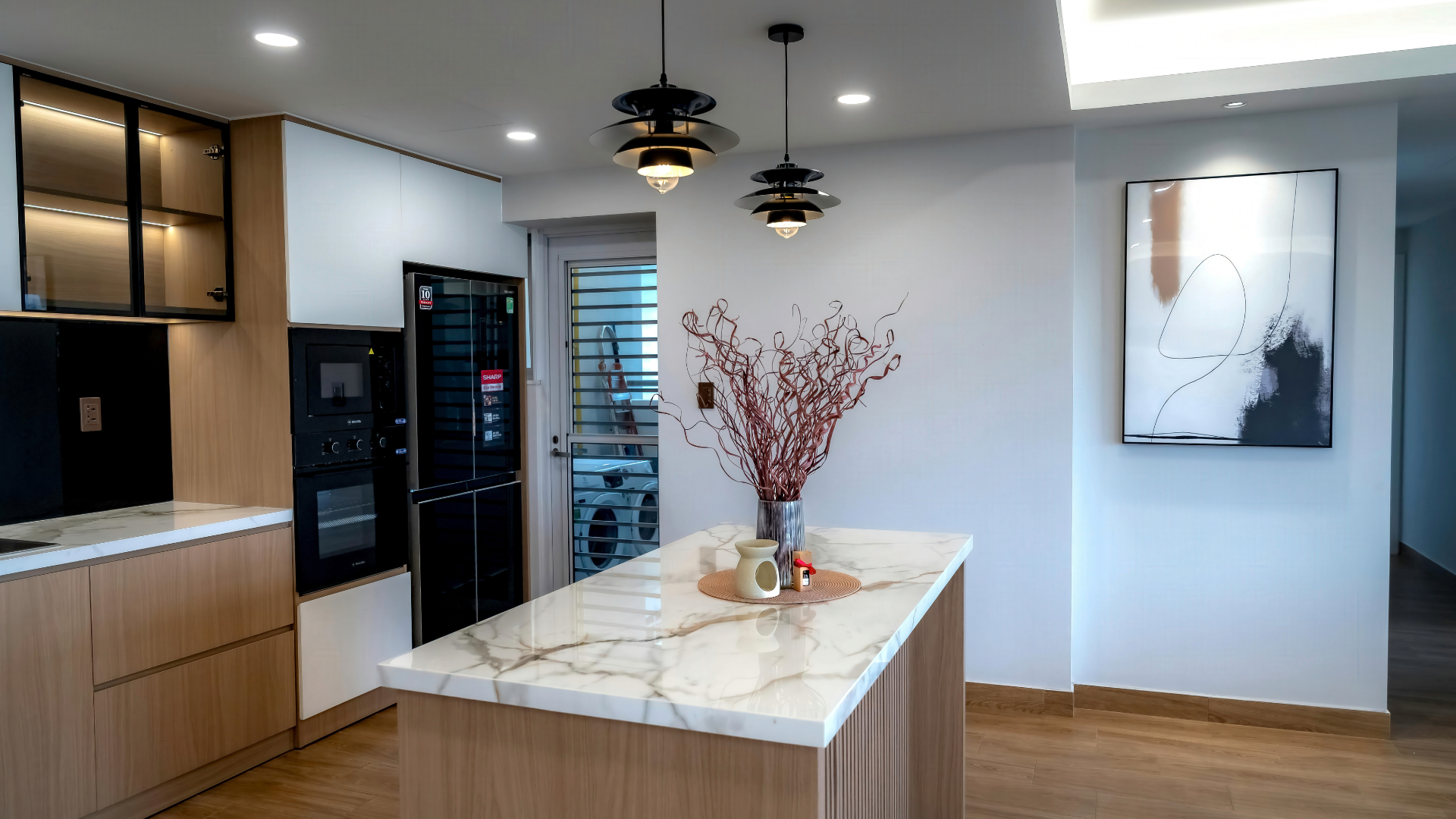 Modern kitchen with island, marble countertop, wooden cabinets, two pendant lights, and art.