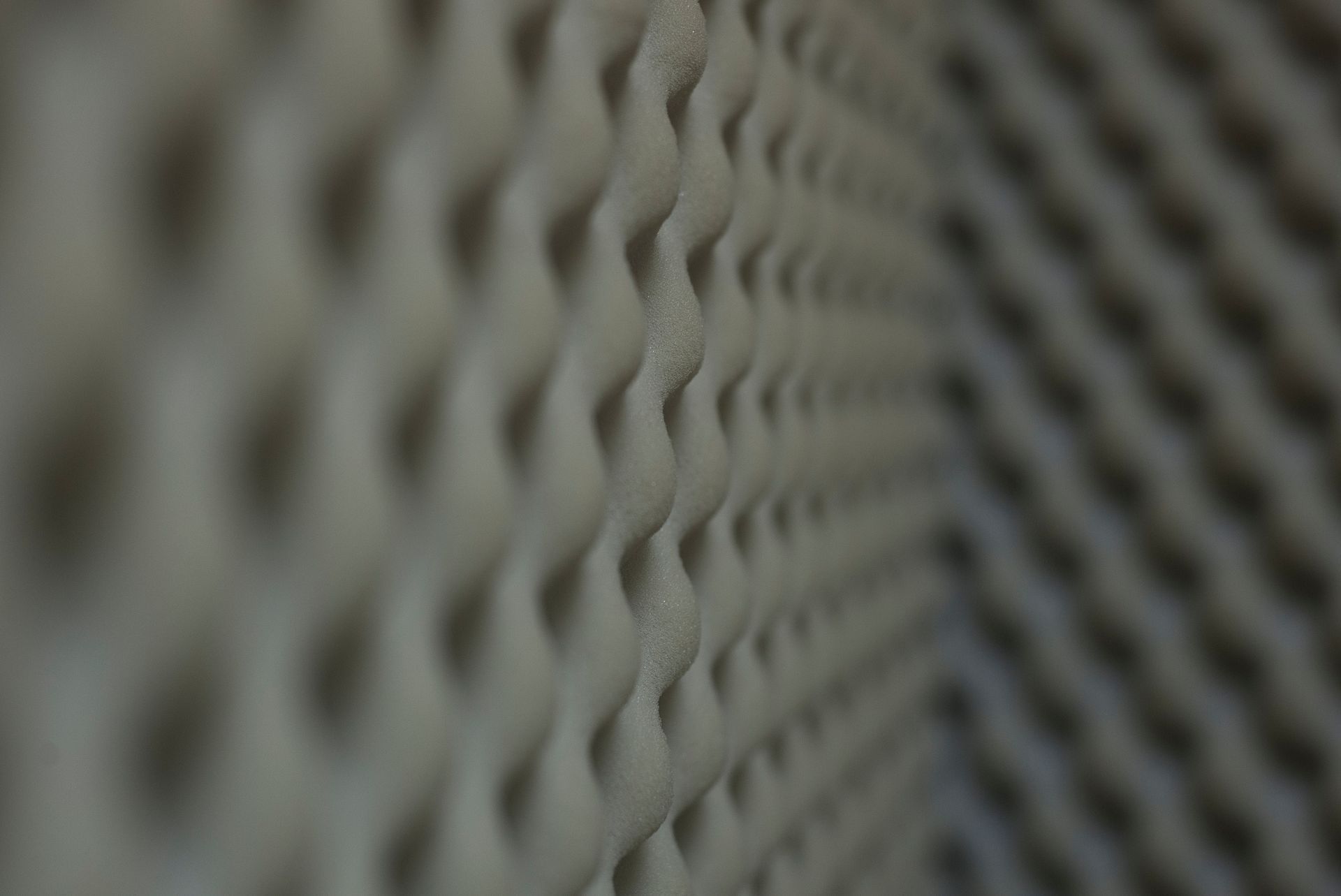Close-up of a beige acoustic foam panel, the surface covered in wave-like protrusions, angled perspective.