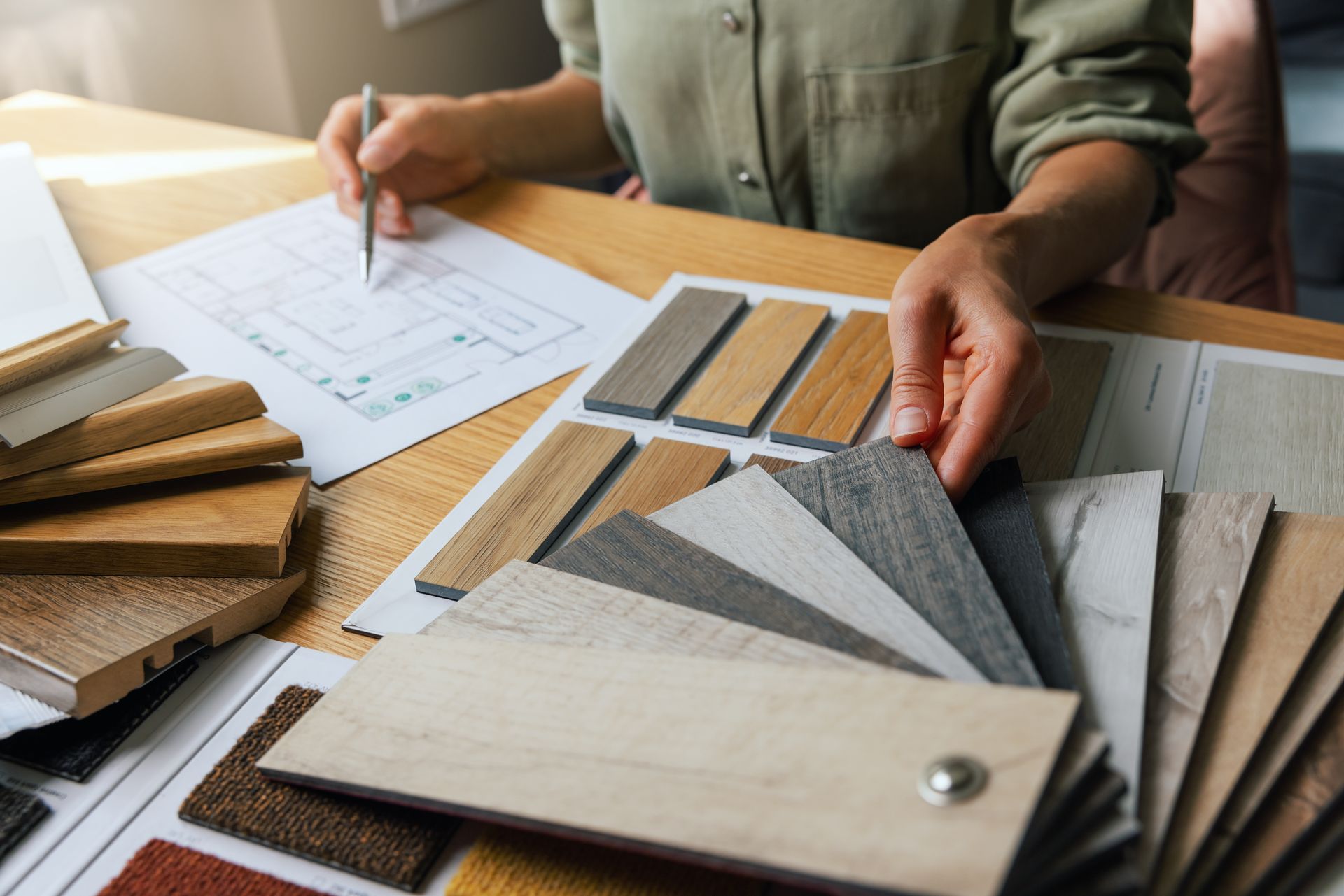Person holding wood samples, sketching on a floor plan, selecting materials for a design project.