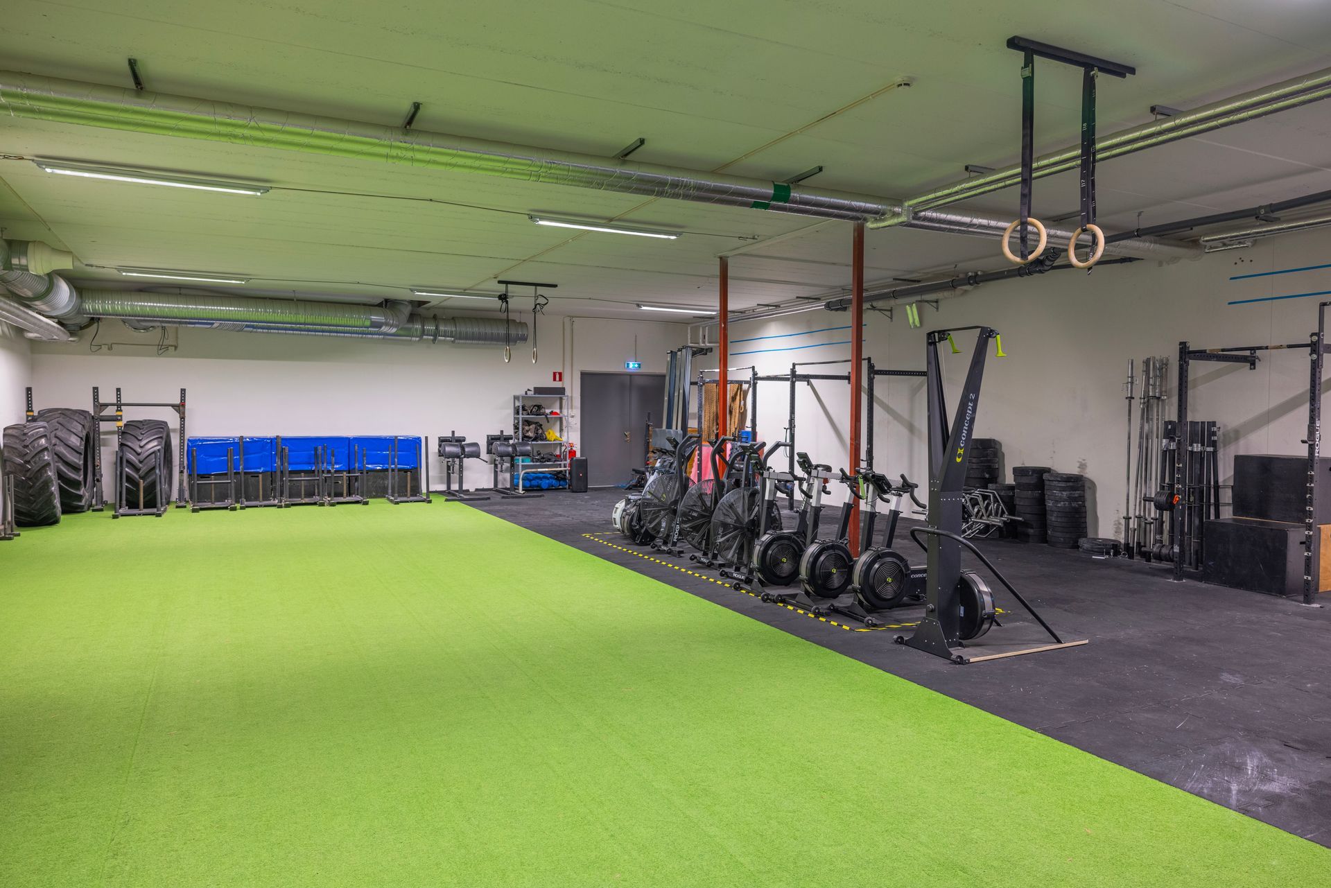 Gym interior with green turf, black equipment, and workout machines.