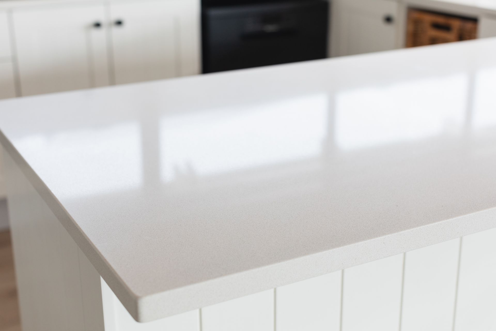White quartz countertop on a kitchen island with white cabinets and black appliances.