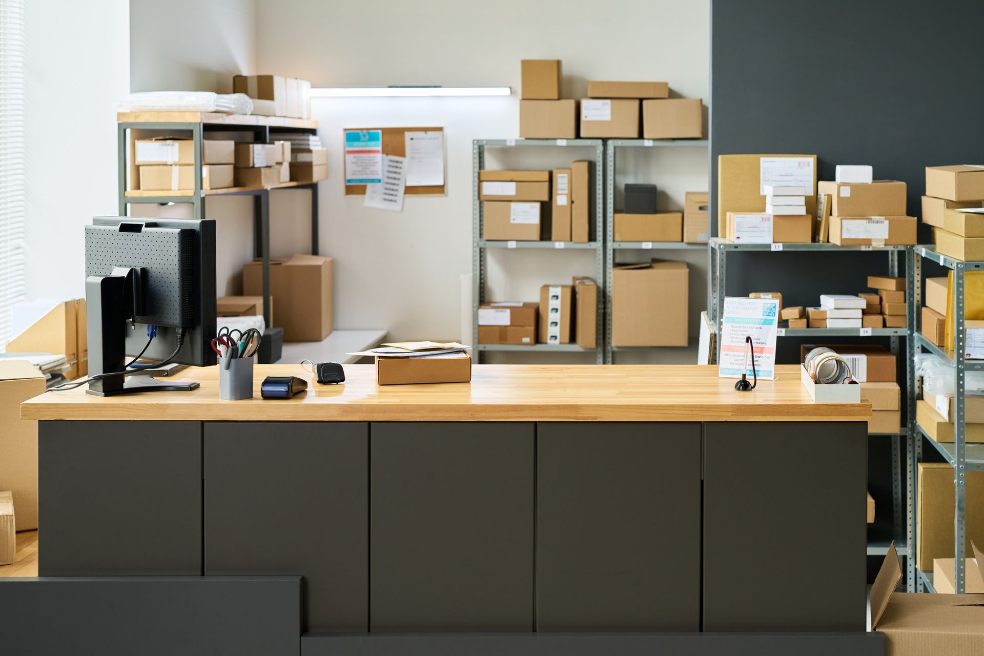 Shipping station with desk, computer, shelves filled with packed cardboard boxes.