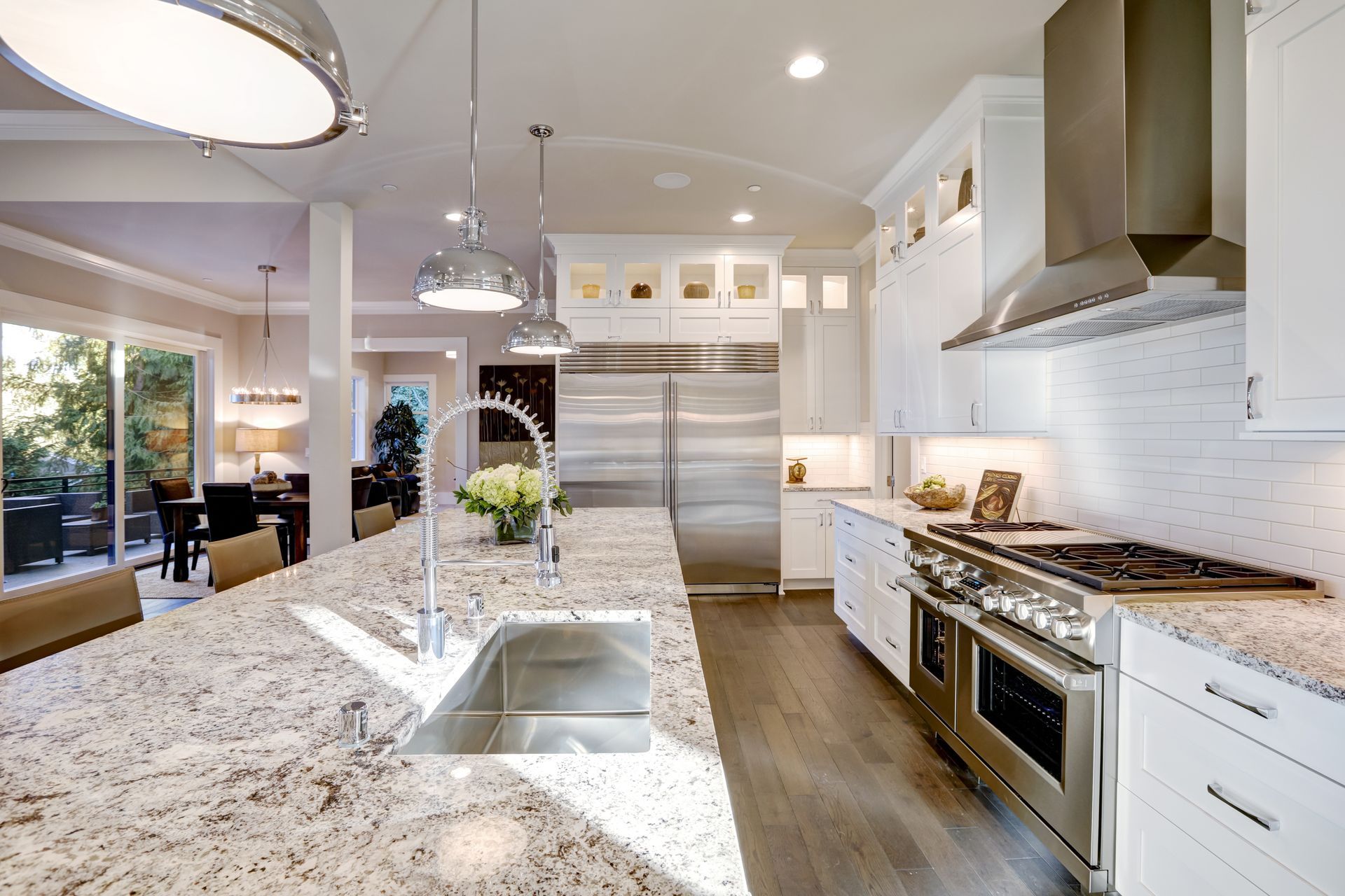 Modern white kitchen with granite countertops, stainless steel appliances, and island sink.