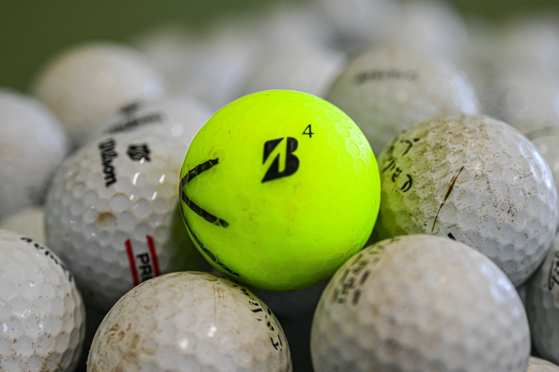 A yellow golf ball is sitting on top of a pile of white golf balls.