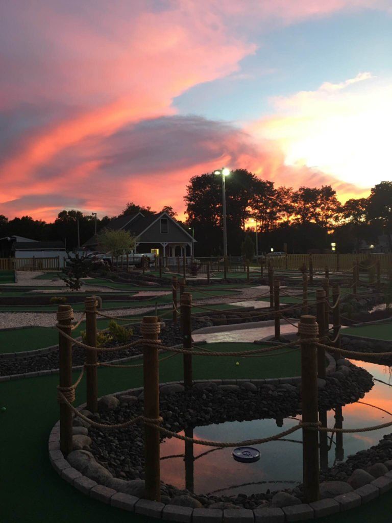 A sunset over a golf course with a pond in the foreground.