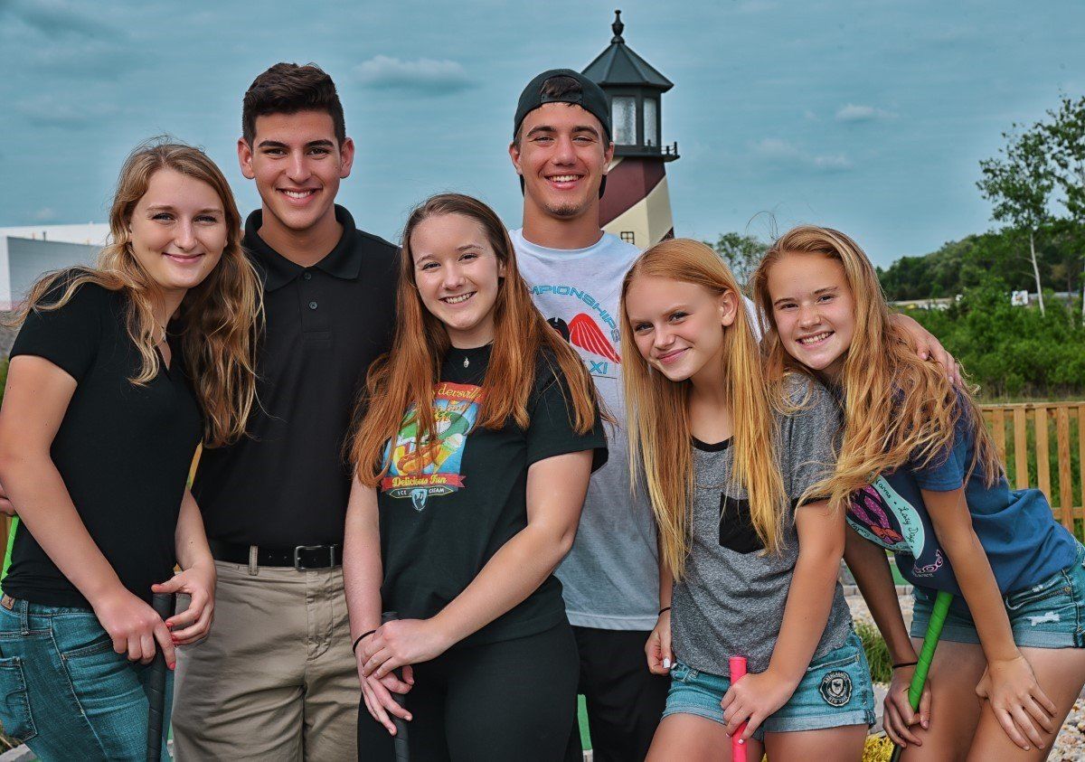 A group of young people are posing for a picture in front of a lighthouse.